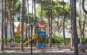 Explore the park's play area, featuring a colorful play structure with a slide and climbing elements, surrounded by tall trees and benches.