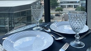 Een eettafel met borden, bestek en een glas op een balkon met uitzicht op een stadslandschap met hoge gebouwen.