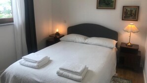 Una cama bien tendida con dos toallas blancas dobladas, un cabecero oscuro y dos lámparas de noche.