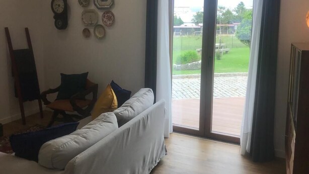 Una sala de estar con sofá, una silla y una mesa de centro. Hay un ventanal corredero que da a un espacio exterior.