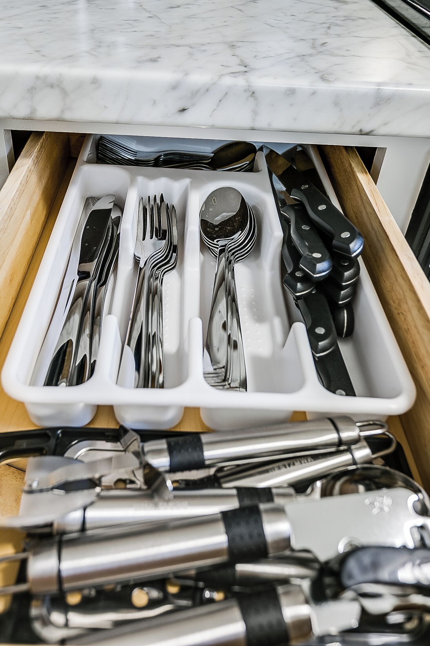 Eine Schublade mit ordentlich sortierten Küchenutensilien, darunter Gabeln, Löffel, Messer und ein Dosenöffner.