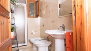 A bathroom with a wooden door, a white sink, two toilets, and a shower. - [Dimora dell'Arco] Seaside Apartment with Stunning Views (Orosei)