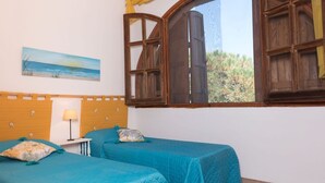 A bedroom with two beds, a wooden headboard, a painting of a beach, and a window with wooden shutters. - [Dimora dell'Arco] Seaside Apartment with Stunning Views (Orosei)