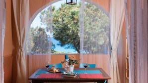 A dining area with a table set for two, a view of trees through a large window, and a bottle of wine. - [Dimora dell'Arco] Seaside Apartment with Stunning Views (Orosei)