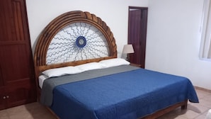 Un dormitorio con cabecera de madera, colcha azul y un papel tapiz estampado detrás de la cabecera.