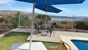 Un patio con mesa y sillas, piscina y vistas a un lago y colinas.