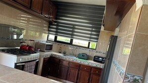 Una cocina con estufa a gas, microondas, tostadora y una ventana con persianas.