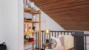 A cozy reading nook with a wooden ceiling, a cushioned chair, and a bookshelf filled with books and decorative items.