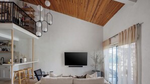 A modern living room with a flat-screen TV, a wooden ceiling, and a balcony with a railing.