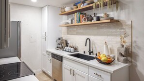 A modern kitchen with white cabinetry, a black countertop, and a built-in stove. There are shelves above the sink holding books and decorative items.