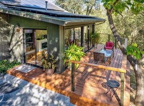 A modern house with a deck, a glass door entrance, and outdoor furniture. - Spacious Mountain View Home - Pool, Spa, Game Room & Stunning Views [Sleeps 13] (Oakhurst)