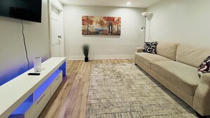 Un salon moderne avec un téléviseur à écran plat fixé au mur, un canapé beige, un tapis à motifs et une petite plante en pot.