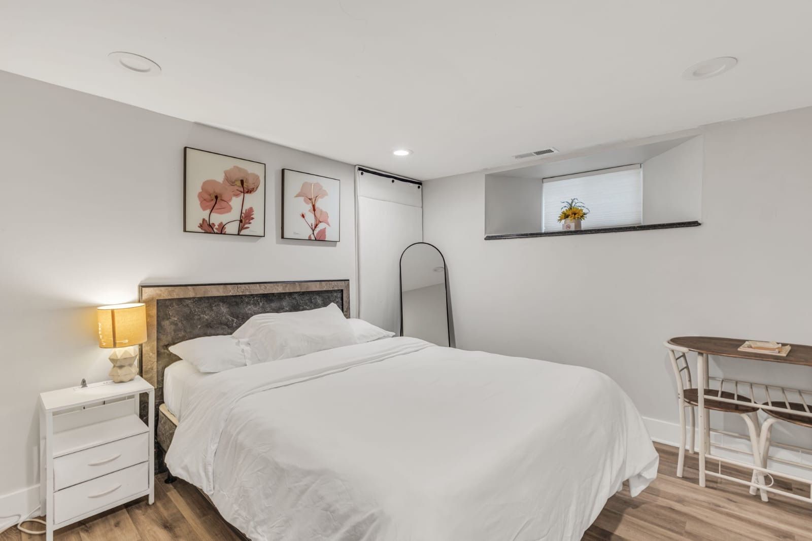 A modern bedroom with a bed, bedside table, lamp, and a small desk with a chair.