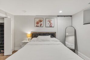 Un dormitorio moderno con cama, mesita de noche, lámpara y dos cuadros enmarcados con motivos florales.