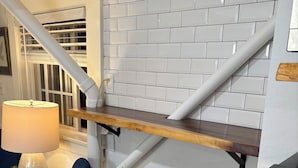 Et køkken med hvide metrofliser, en træhylde, en blå stol og en lampe.