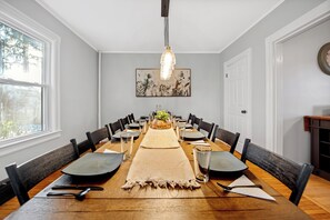 A dining room with a long wooden table, black chairs, and a central floral arrangement. - Spacious 5-Bedroom Home with Game Room in Amherst - Mins to UMass (Amherst)