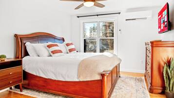 A bedroom with a wooden bed, a ceiling fan, a window with blinds, a dresser, and a television on the wall.
