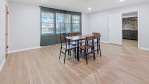 Un comedor con una mesa y sillas de madera, un ventanal con cortinas y vista a un muro de ladrillo.