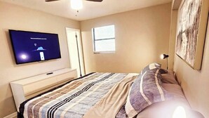 Une chambre à coucher avec un lit, un ventilateur de plafond, une télévision, une fenêtre et un tableau au mur.
