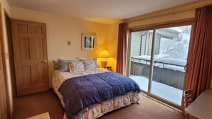 A bedroom with a bed, a nightstand, a lamp, a chair, and a sliding glass door to a balcony. - Cozy condo, next to the ski slopes with 2 private balconies (Whitefish)