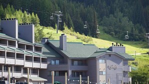 A hotel with multiple balconies, a ski lift in the background, and a forested hillside. - Cozy condo, next to the ski slopes with 2 private balconies (Whitefish)