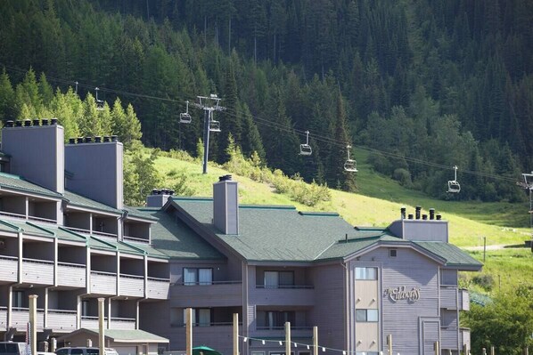 A hotel with multiple balconies, a ski lift in the background, and a forested hillside. - Cozy condo, next to the ski slopes with 2 private balconies (Whitefish)