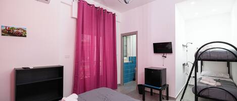 A bedroom with a bunk bed, a flat-screen TV, a desk, and a window with curtains.