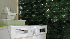 A white washing machine with a control panel and a small shelf on top. - Splendori Rooms (Palermo)