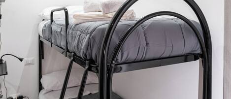 A bunk bed with grey bedding and black metal frame, white walls, and a tiled floor.