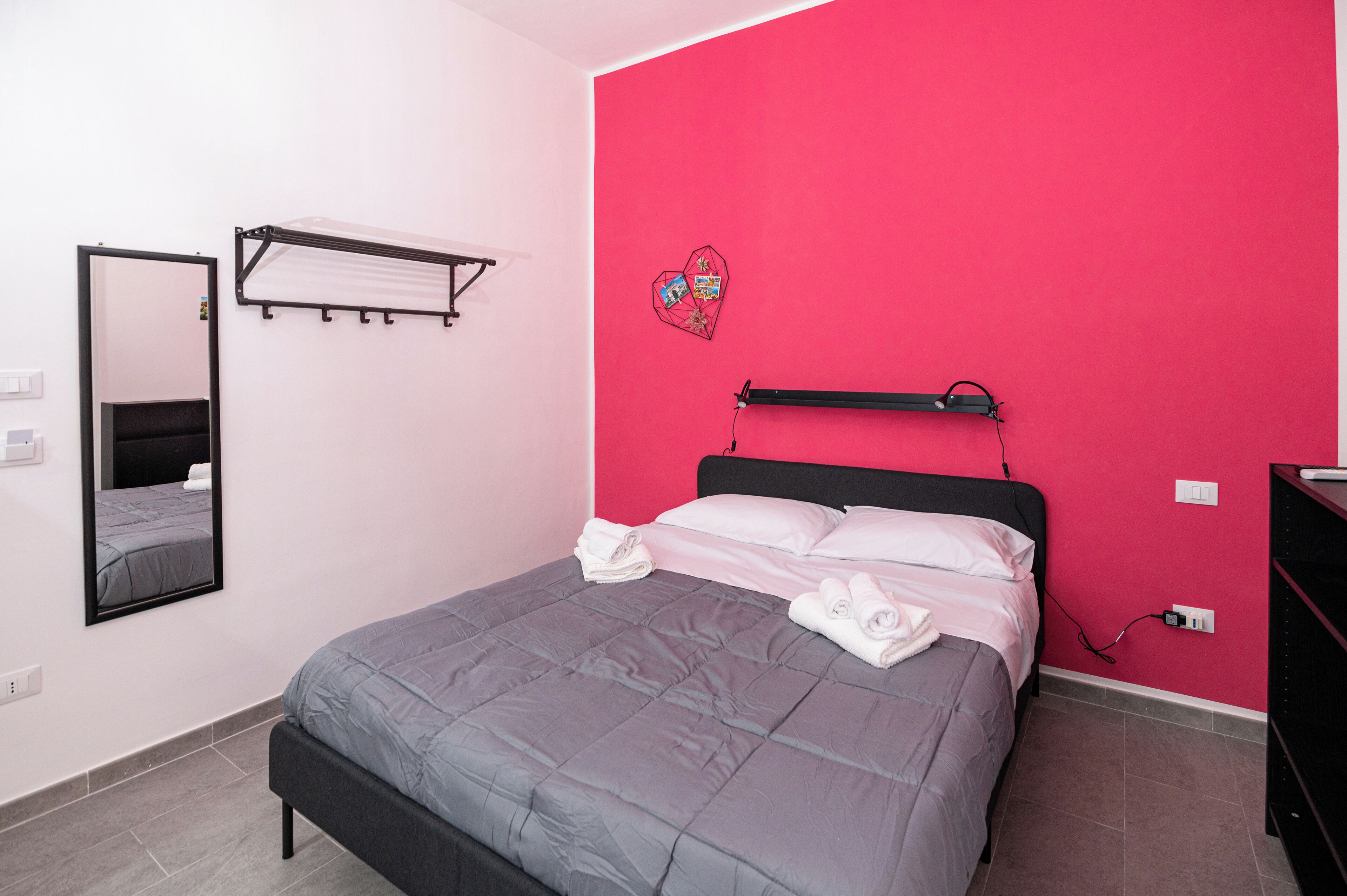 A bedroom with a bed, a mirror, a shelf, and a red wall.