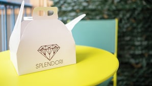 A white paper bag with a diamond design and the word "SPLENDORI" on it, placed on a yellow table. - Splendori Rooms (Palermo)