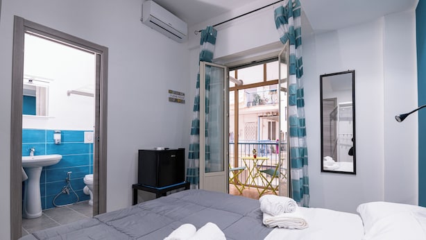 A hotel room with a bed, a TV, a bathroom with a sink and toilet, and a balcony with a chair and table. - Splendori Rooms (Palermo)