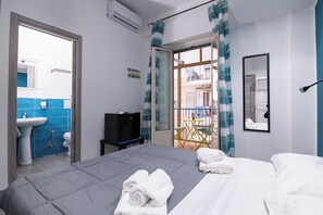A hotel room with a bed, a TV, a bathroom with a sink and toilet, and a balcony with a chair and table. - Splendori Rooms (Palermo)