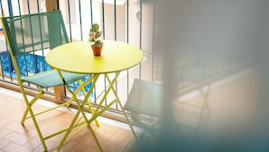 A yellow table with a potted plant on a balcony with a green chair. - Splendori Rooms (Palermo)
