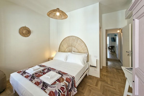 A bedroom with a bed, bedside lamps, a woven headboard, and a wooden floor.