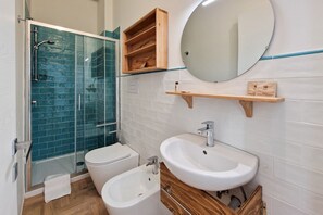 A bathroom with a glass shower enclosure, a toilet, a bidet, a sink, and a mirror.