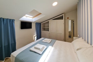 Ein Schlafzimmer mit Bett, Dachfenster, Fernseher, Kleiderschrank und Spiegel.