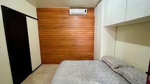 A bedroom with a wooden panel wall, a bed with patterned bedding, and a white wardrobe. - AP 08A Ala Morrinhos Residencial Solavir (Bombinhas)