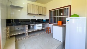 Une cuisine avec un plan de travail noir, des placards blancs, une fenêtre à barreaux et un réfrigérateur blanc.
