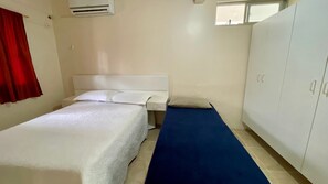 A small, single-bed room with a white headboard, a blue bed runner, a white wardrobe, and a red curtain.