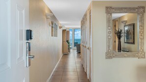 Un pasillo de hotel con diseño moderno, que presenta un largo corredor, un espejo decorativo y vistas del cielo a través de las ventanas.