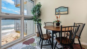 Un área de comedor con vista a la playa, una planta en maceta y un letrero decorado con motivos playeros en la pared.