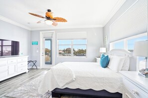 Une chambre à coucher avec un lit, un ventilateur de plafond, une fenêtre donnant sur un beau paysage, une commode et une porte.