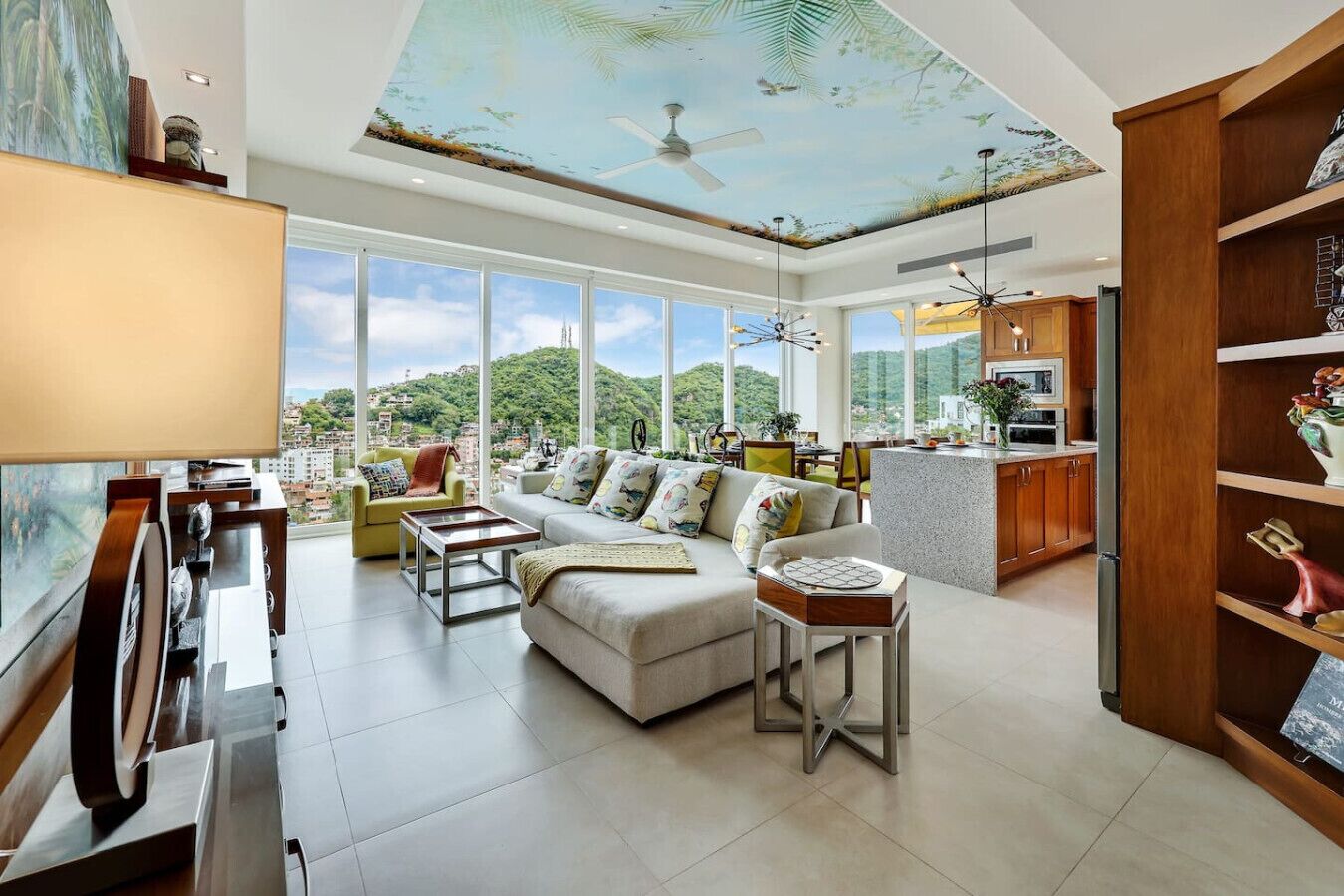 A spacious living area with a large window, a ceiling fan, and a kitchen area with wooden cabinets.