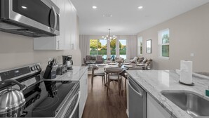 Una cocina moderna con electrodomésticos de acero inoxidable, un comedor con encimera de mármol y vistas a una piscina a través de amplias ventanas.