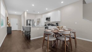 Una cocina moderna con armarios blancos, una isla central y un comedor con una mesa redonda y seis sillas.