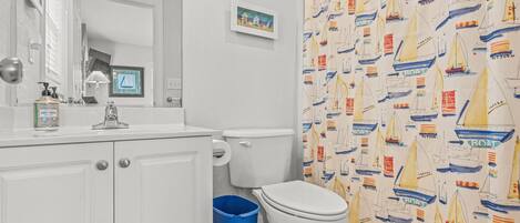 Un baño con lavamanos blanco, inodoro y cortina de ducha con temática náutica.