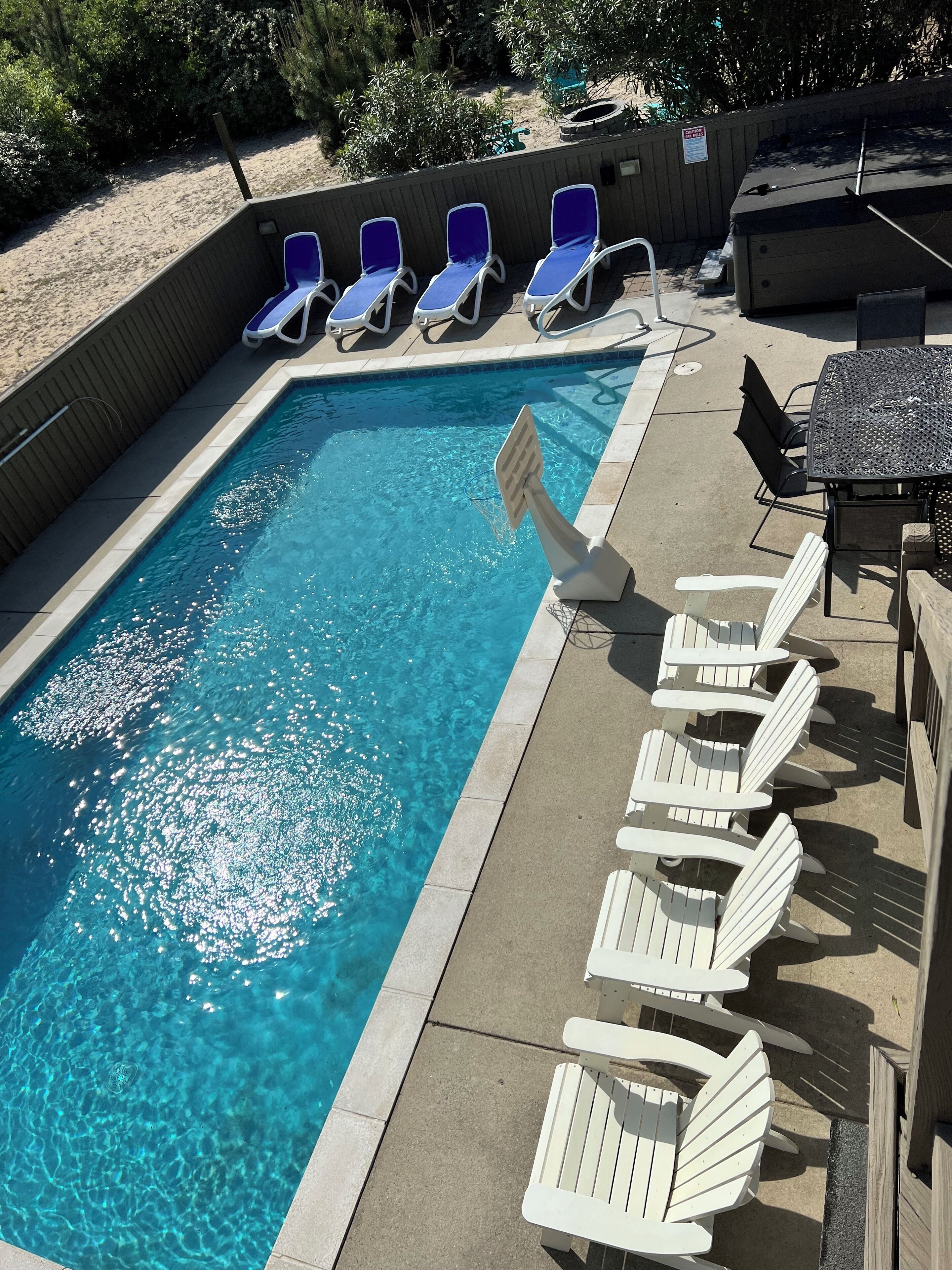 A swimming pool with blue and white lounge chairs, a table, and a covered area with a sign.