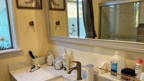Un baño con lavamanos de mármol, un espejo y diversos artículos de aseo sobre la encimera.