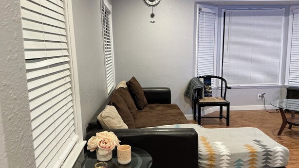 Una sala de estar con un sofá, una mesa de centro de vidrio, una mesita auxiliar con un florero y una taza, y un plaid decorativo en el sofá.